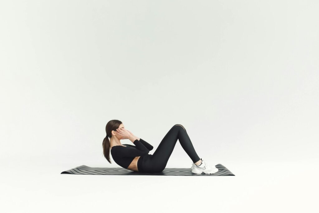 Woman in activewear doing sit-ups on yoga mat in bright studio setting.